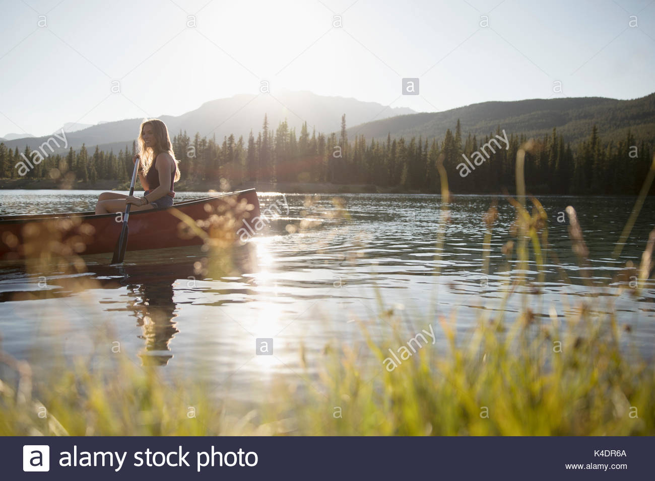 Donna paddling canoe con remo sulla soleggiata tranquilla estate lago Foto Stock