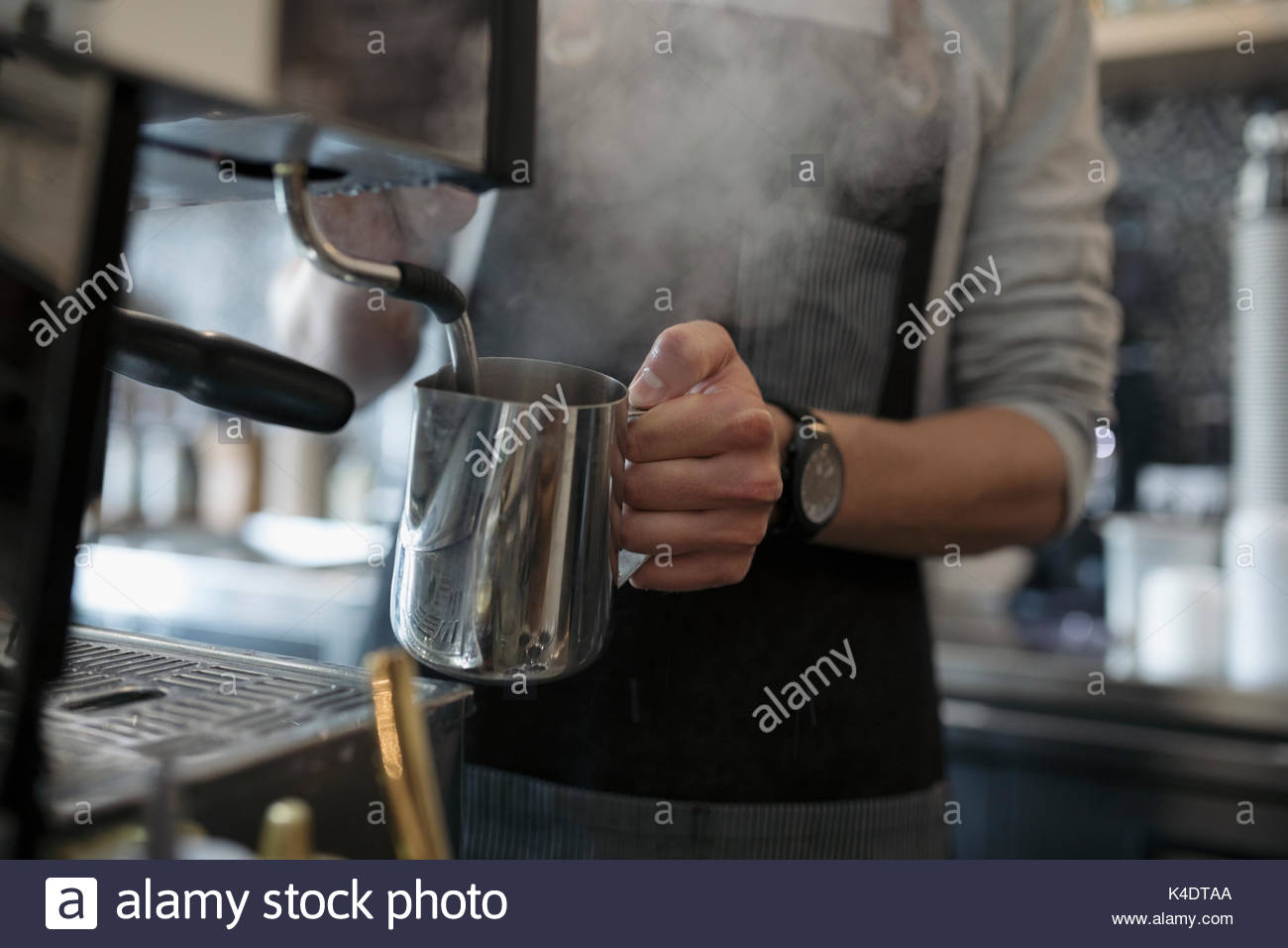 Barista maschio della cottura a vapore di latte a macchina espresso in cafe Foto Stock