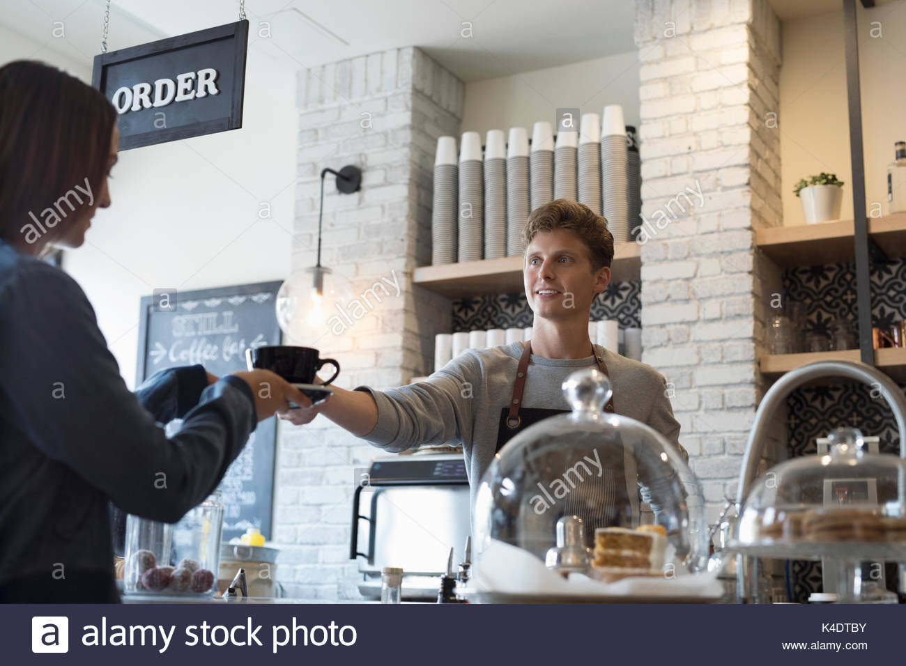 Voce maschile barista che serve caffè al cliente femmina in cafe Foto Stock