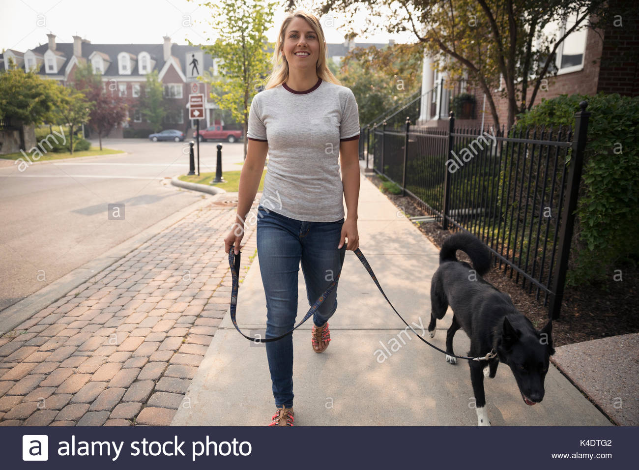 Donna sorridente walking cane al guinzaglio sul marciapiede di vicinato Foto Stock