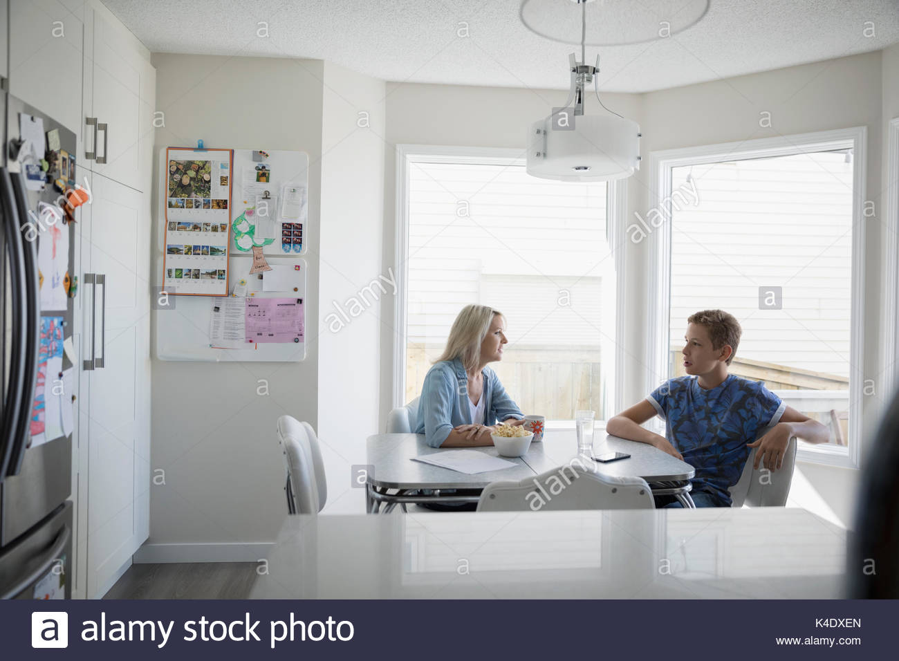 Madre e pre-adolescenti figlio di parlare al tavolo della cucina Foto Stock