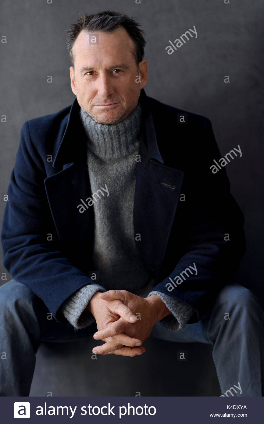 Ritratto fiducioso uomo maturo in turtleneck maglione e rivestire contro uno sfondo grigio Foto Stock