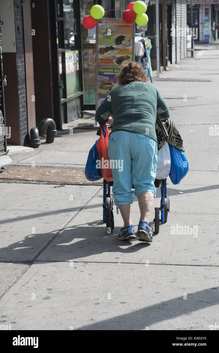 Donna anziana con molte borse spinge lungo il marciapiede appoggiato su di un walker in Brooklyn, New York. Foto Stock