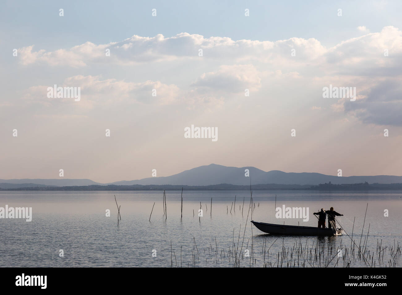 Due pescatori su una piccola barca con una rete da pesca, con belle sfumature calde e distante dei raggi solari Foto Stock