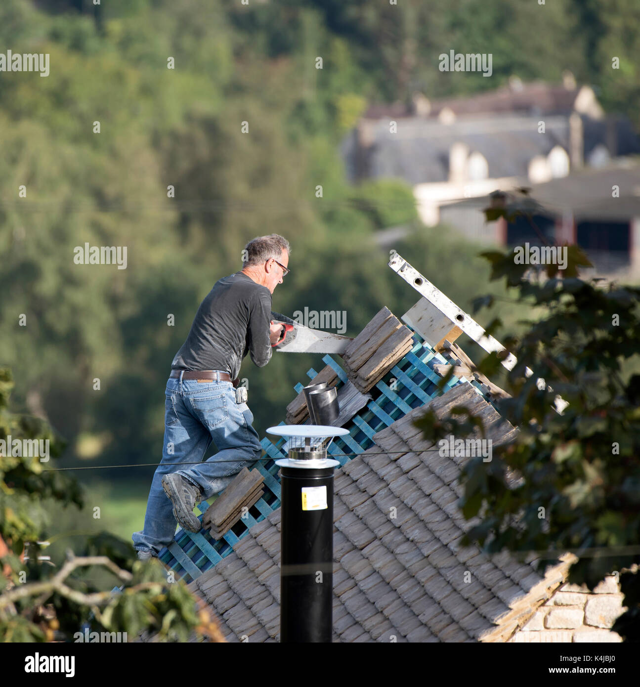 Panoramica di un builder usando una sega per tagliare tegole del tetto come il lavoro di costruzione si avvicina al completamento. Foto Stock