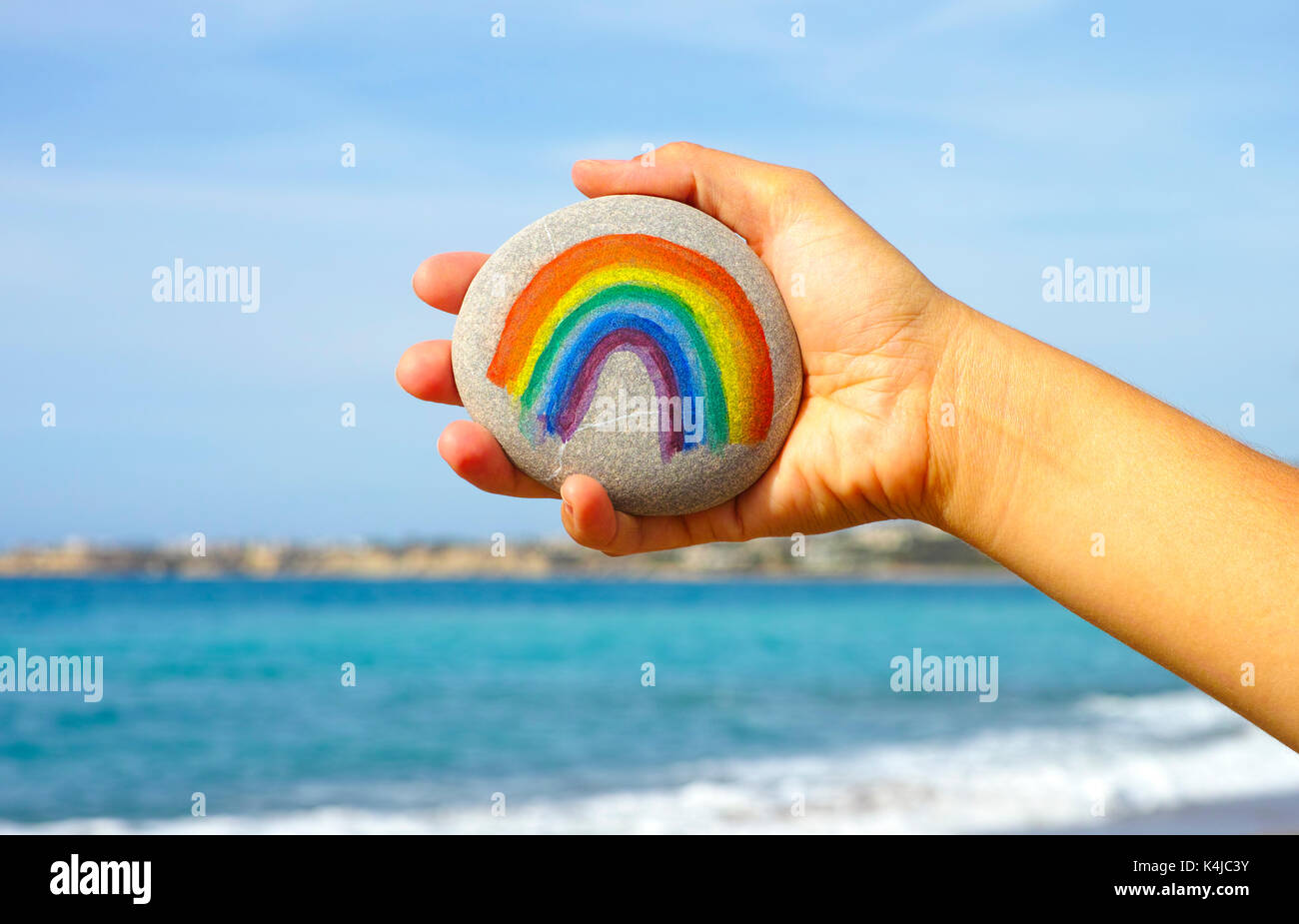 Donna mano azienda sassi con dipinto di rainbow contro il blu del cielo e del mare. Foto Stock