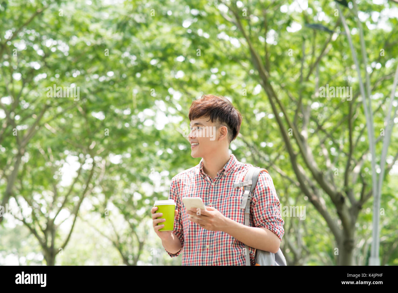 Giovane uomo asiatico sorridente e utilizzando il telefono in posizione di parcheggio Foto Stock