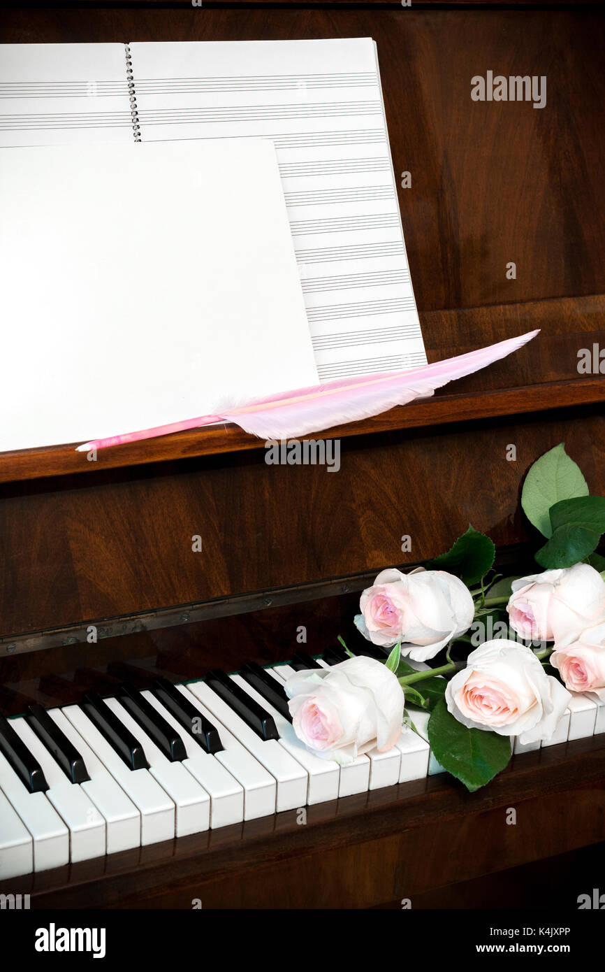 Pianoforte, rosa pallido roses sulla tastiera, carta da musica e vuoto bianco con cappello rosa penna. Foto Stock