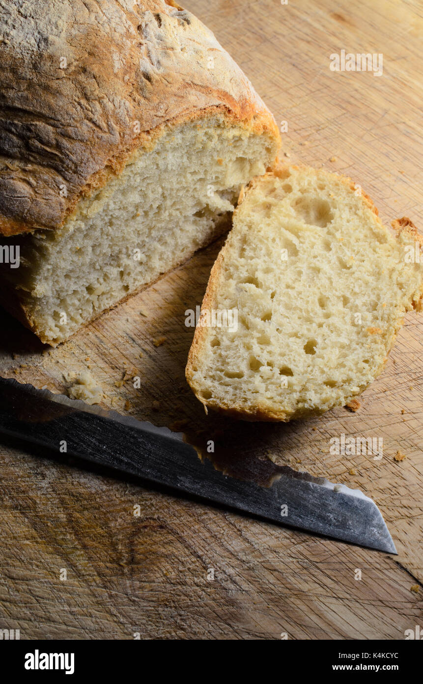 Pane appena sfornato pagnotta di pane, ripresa dall'alto. prima fetta tagliata e disteso a faccia in su sul tagliere di legno con lama di coltello. Foto Stock