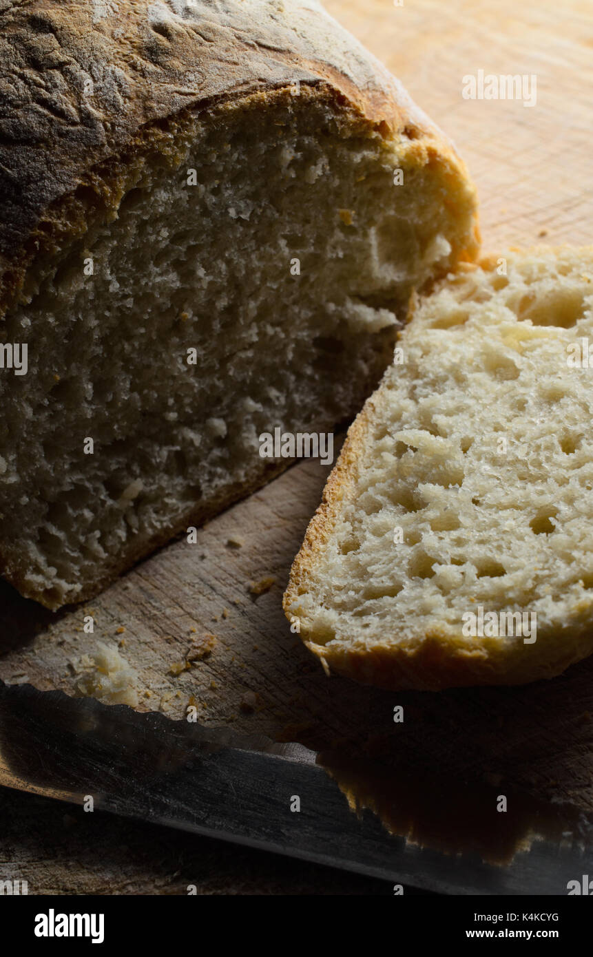 Pane appena sfornato pagnotta di pane, con la prima fetta tagliata e disteso a faccia in su sul tagliere di legno con lama di coltello. Foto Stock