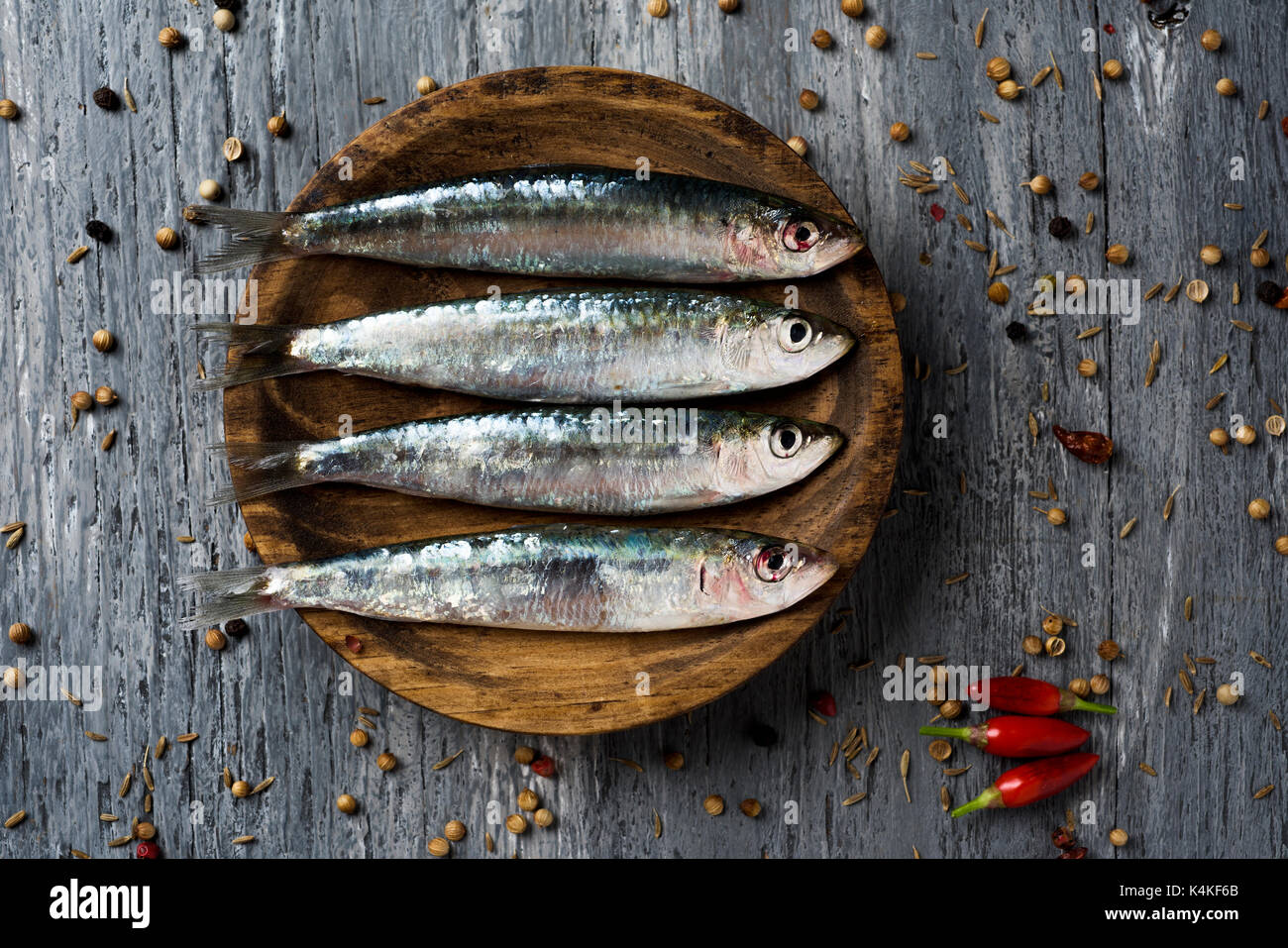 Alta angolazione di alcune materie di sardine in un piatto di legno, collocata sul grigio di una tavola in legno rustico cosparsi di pepe Foto Stock
