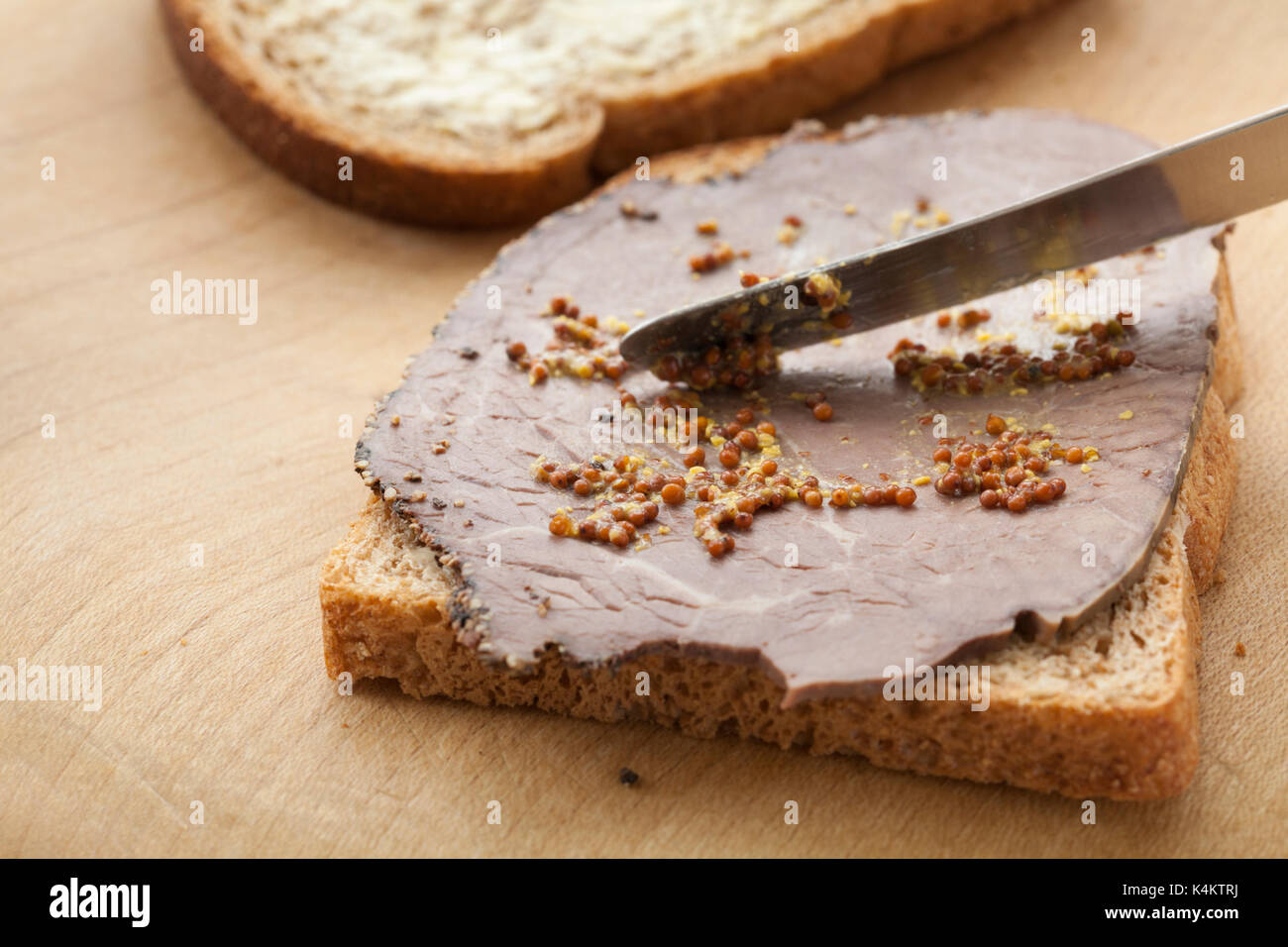 Facendo un sandwich con pane integrale, la carne di manzo britannica con crosta impepato e diffondere con cereali integrali senape. Foto Stock