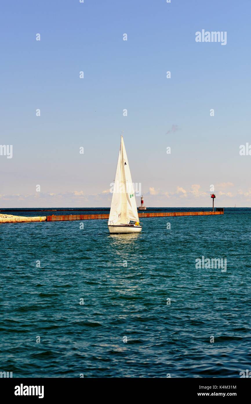 Un lone sailboat rendendo il suo modo dal Lago Michigan in un canale che conduce a Waukegan Harbour su una mattina d'estate. Waukegan, Illinois, Stati Uniti d'America. Foto Stock