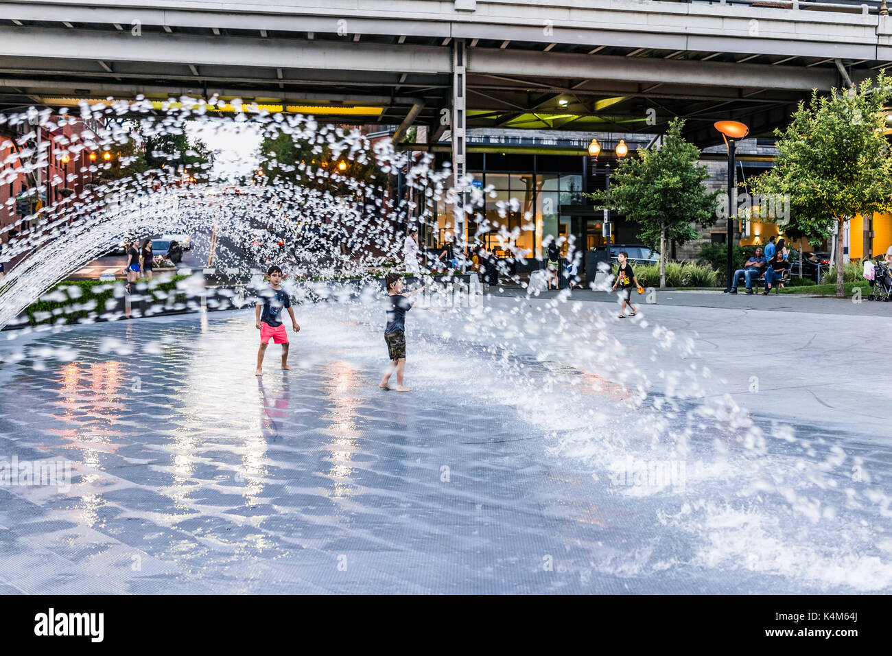 Washington DC, Stati Uniti d'America - 4 Agosto 2017: ragazzi giovani bambini che giocano in acqua Fontana nel parco di Georgetown in serata con spruzzi d'acqua Foto Stock