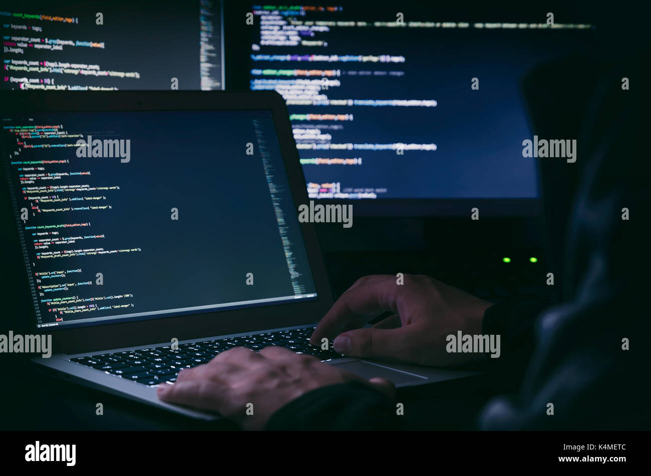 Hacker che lavora su un codice in camera oscura. Il codice di programmazione su schermo. La criminalità su internet concept Foto Stock