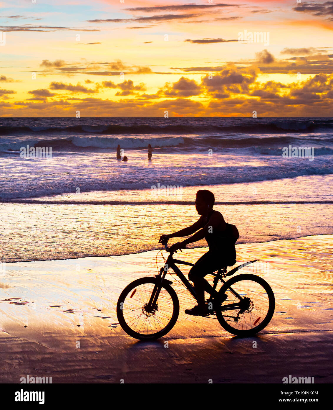 Silhouette di un uomo in sella ad una bicicletta al tramonto sulla spiaggia. L'isola di Bali, Indonesia Foto Stock