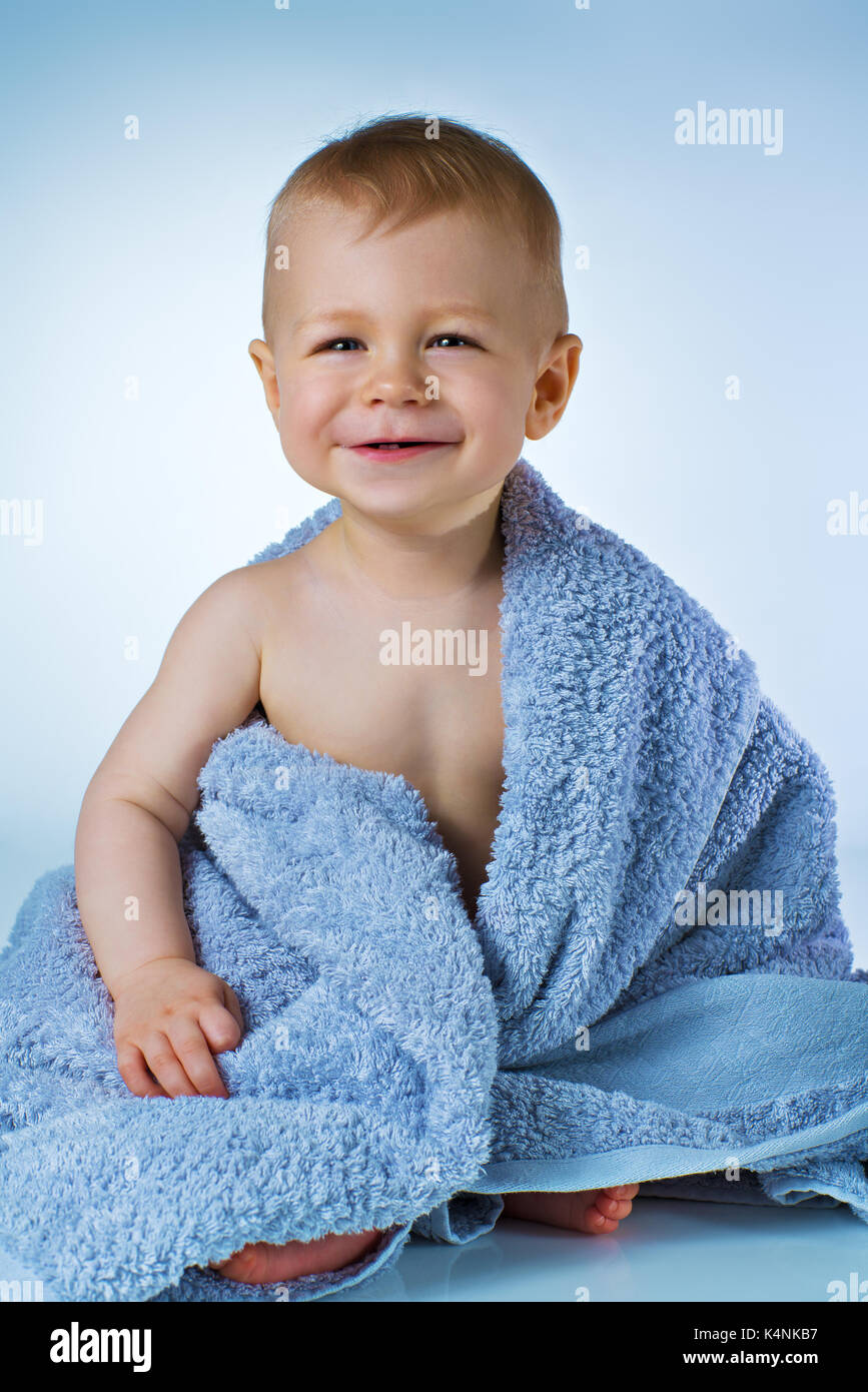 Gli otto mesi baby dopo lavaggio in seduta grande asciugamano morbido e sorridente in bianco e lo sfondo blu Foto Stock