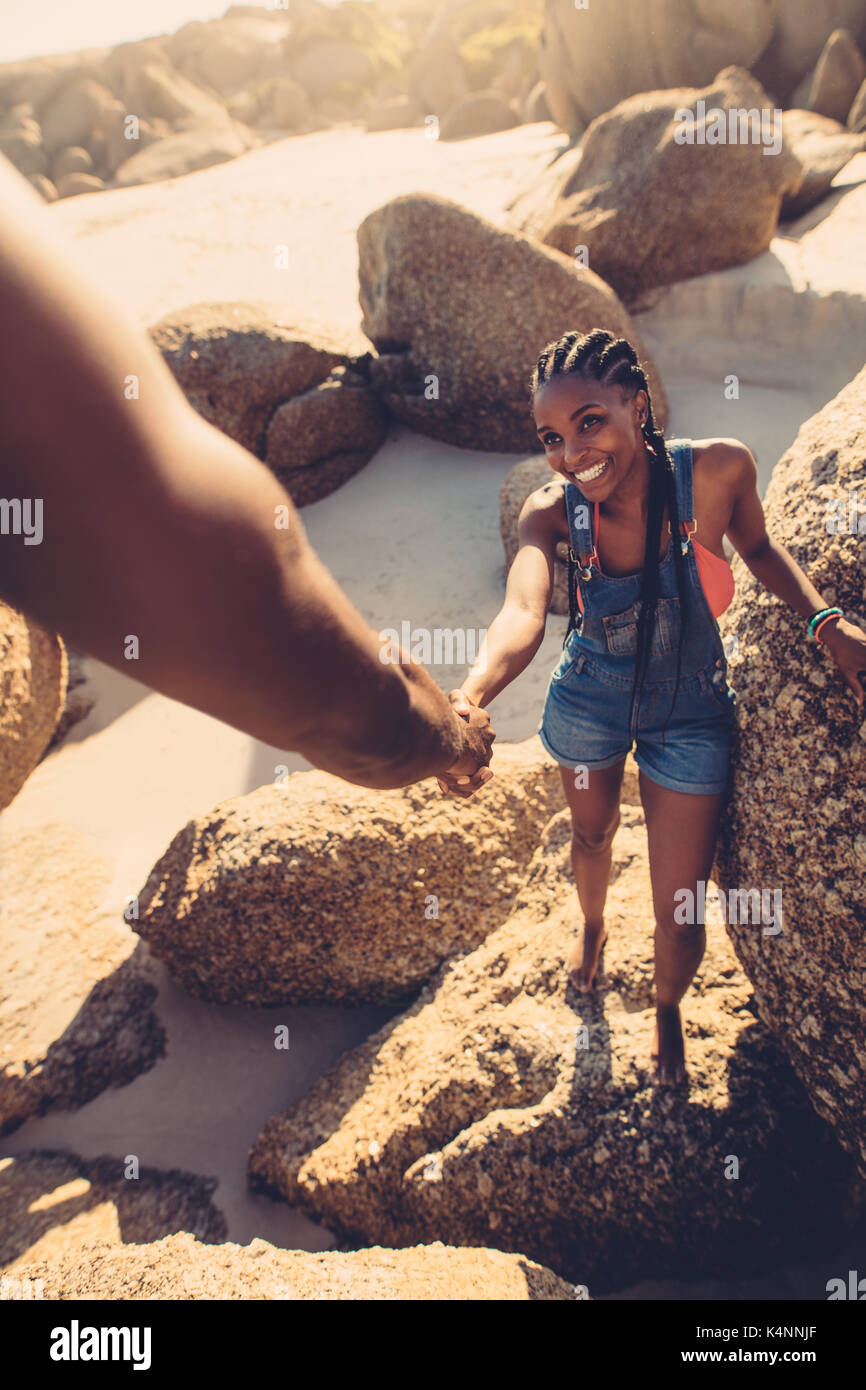 Giovane donna a piedi attraverso le rocce con il supporto dal suo fidanzato. POV shot dell'uomo aiutando la ragazza rock climbing in spiaggia. Foto Stock