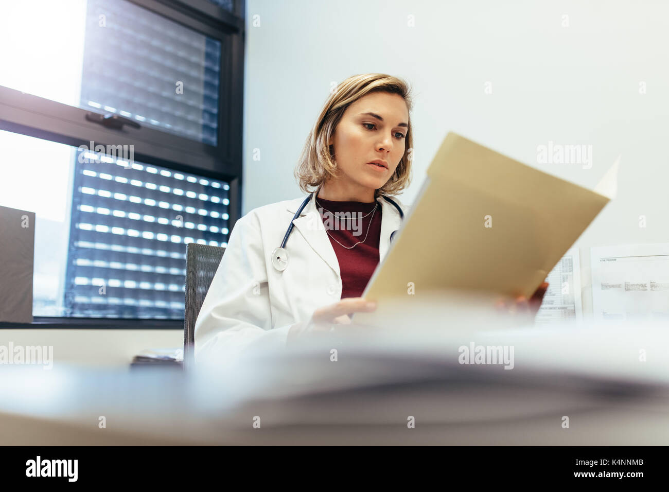 Medico donna seduta nel suo ufficio e studiando i record medici. Medicina professional leggere le relazioni in clinica. Foto Stock