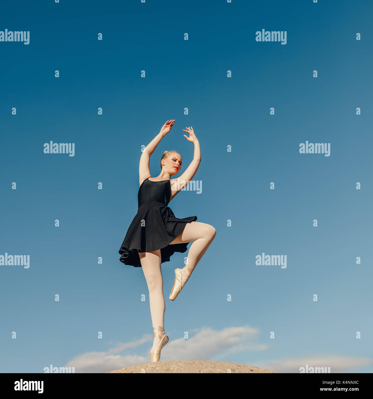 Ballerina praticando la danza si sposta all'esterno. Ballerino femmina in piedi su una punta in pointe shoes su una roccia con cielo blu in background. Foto Stock