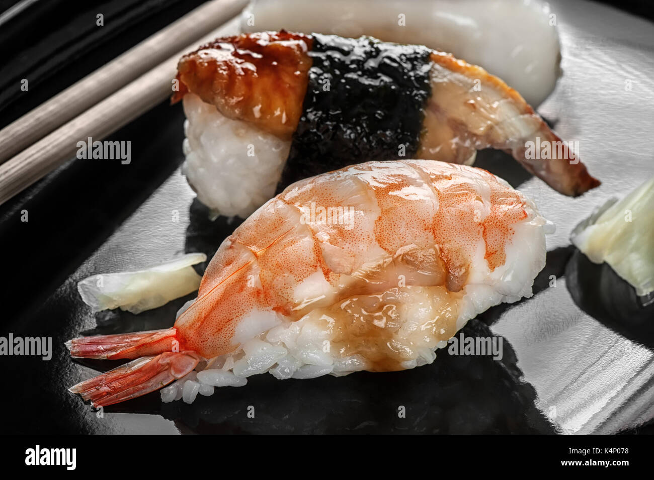 I sushi giapponesi La cucina fatta di riso e di spigola, gamberi e anguilla affumicata con bacchette su una piastra nera. Foto Stock