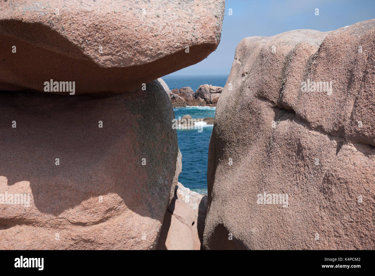 Guardando attraverso una stretta intercapedine tra un affioramento di rosa rocce colorate con il mare sullo sfondo Côte de Granit Rose Bretagna Francia Foto Stock
