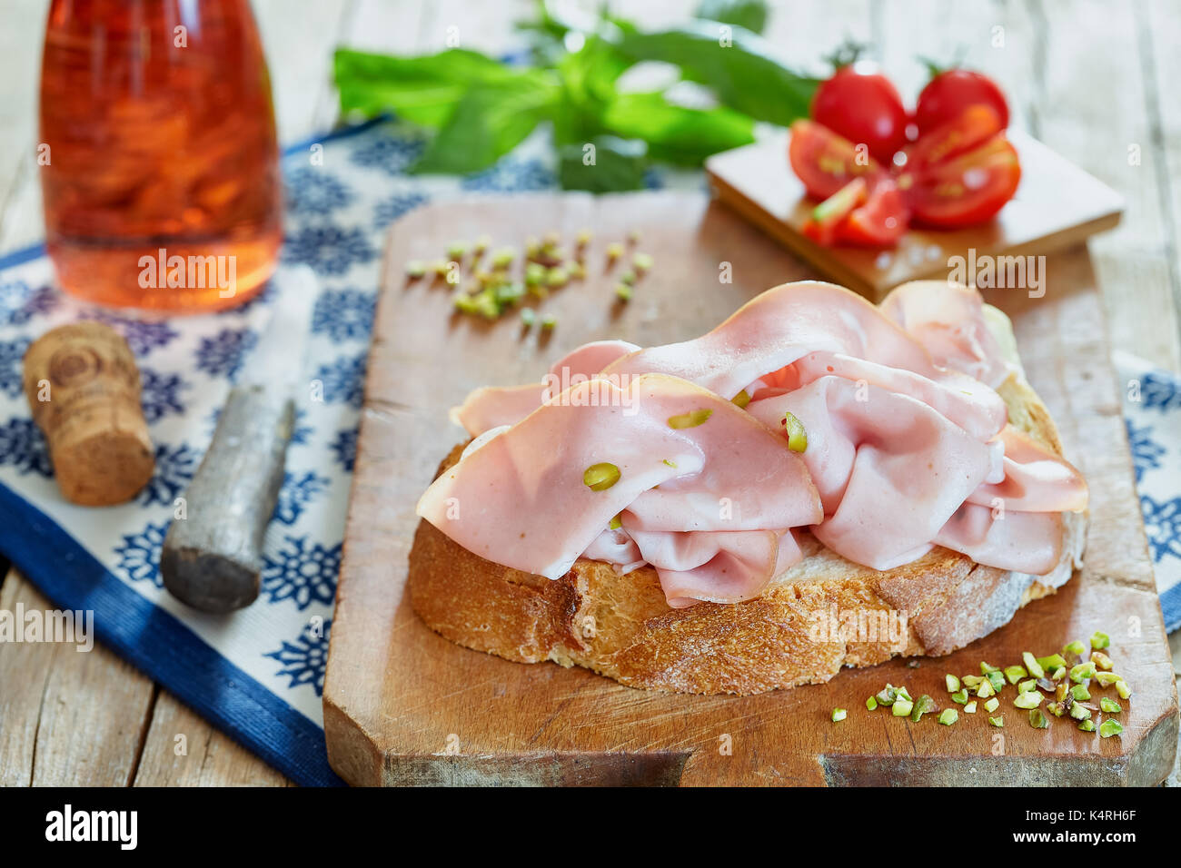 La mortadella con pistacchi freschi sulla fetta di pane con pomodori ciliegia, basilico e rose vino spumante. Foto Stock