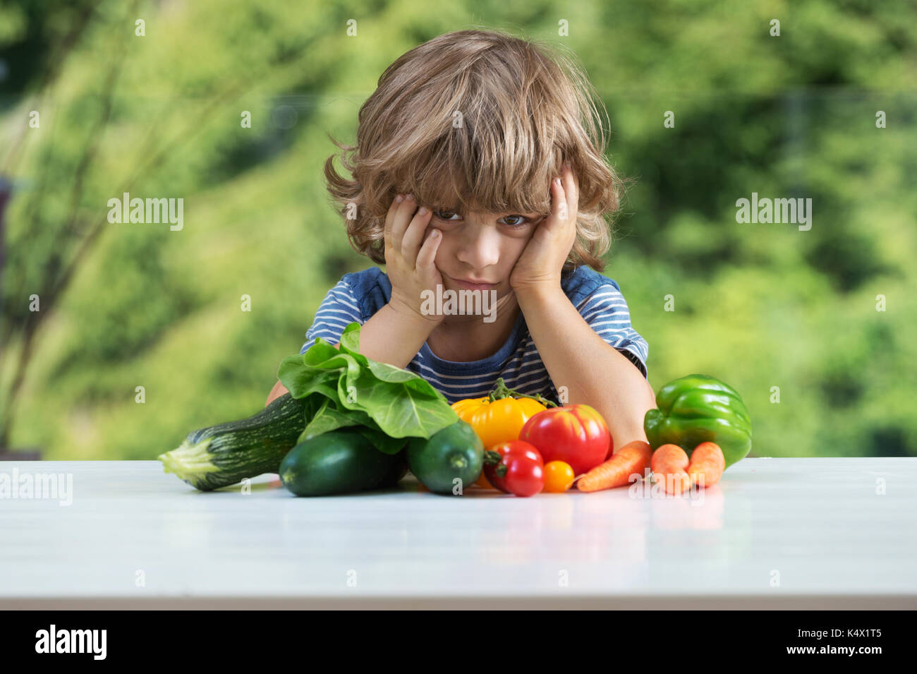 Carino piccolo ragazzo seduto al tavolo, infelice con il suo pasto vegetale, cattive abitudini alimentari, nutrizione e alimentazione sana nozione Foto Stock