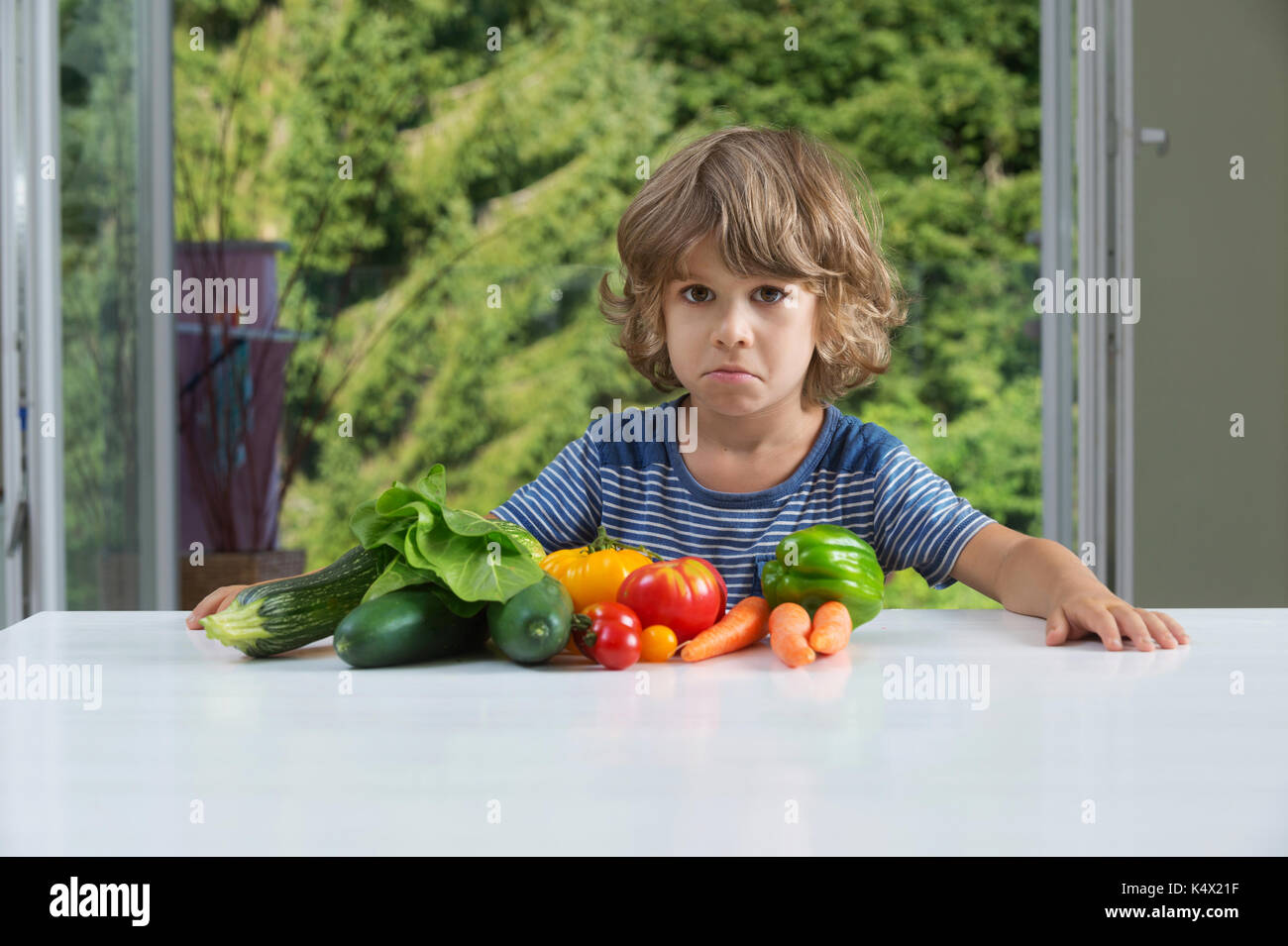 Carino piccolo ragazzo seduto al tavolo, infelice con il suo pasto vegetale, cattive abitudini alimentari, nutrizione e alimentazione sana nozione Foto Stock