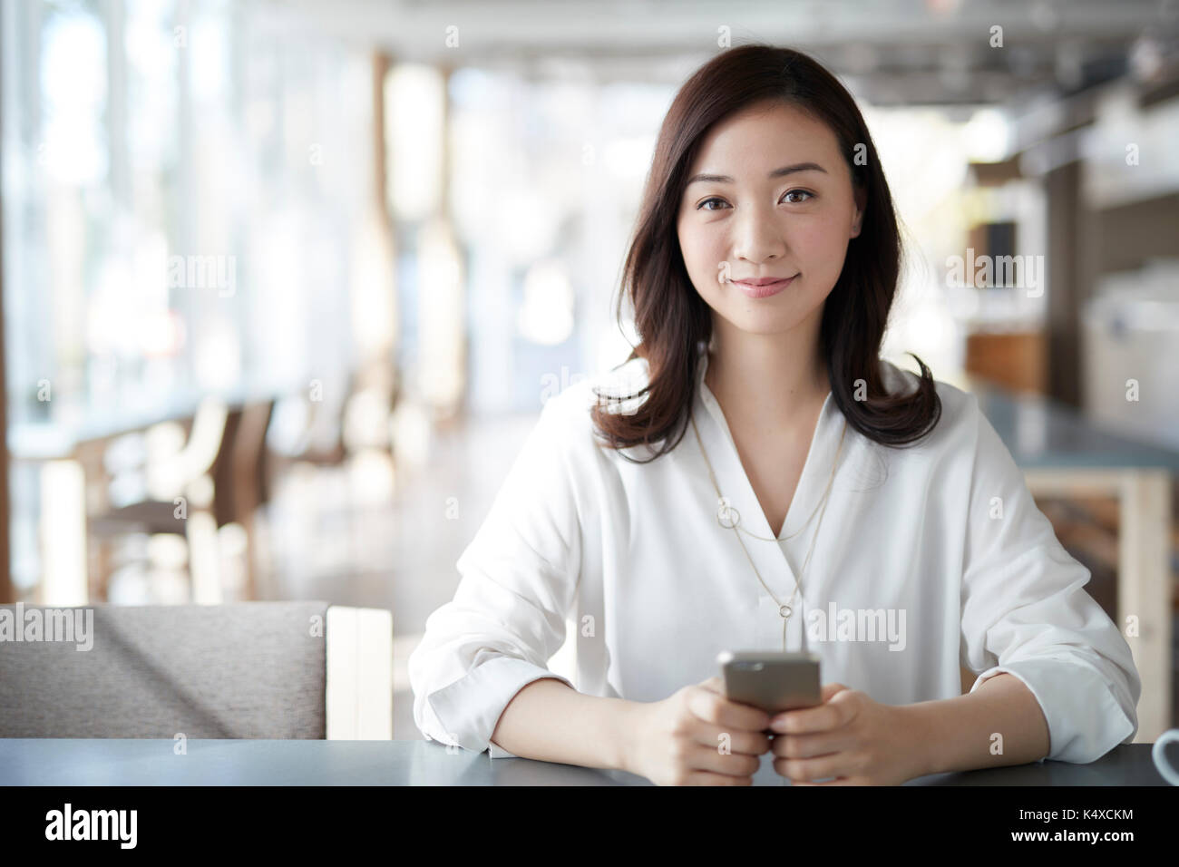 Donna Giapponese con lo smartphone in un elegante cafe Foto Stock