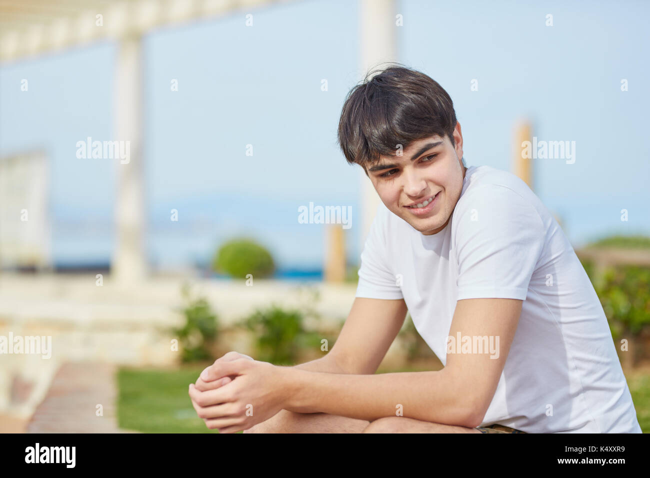 Ritratto di giovane uomo seduto con le mani giunte sorridente Foto Stock