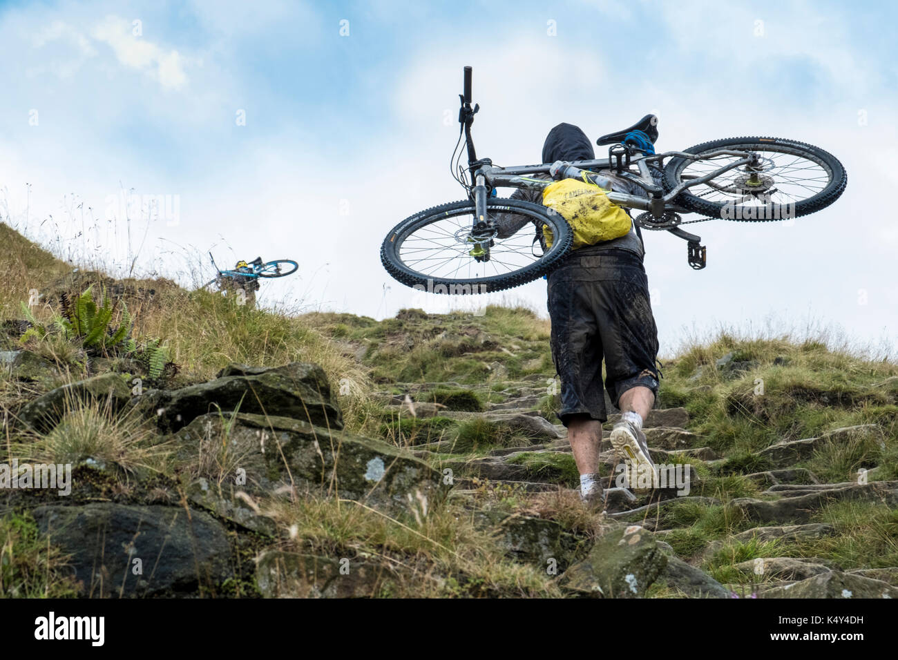 Mountain biker. Ciclista che trasportano una mountain bike fino alla cima di una collina. La scala di Giacobbe, Pennine Way, Derbyshire, Peak District, England, Regno Unito Foto Stock