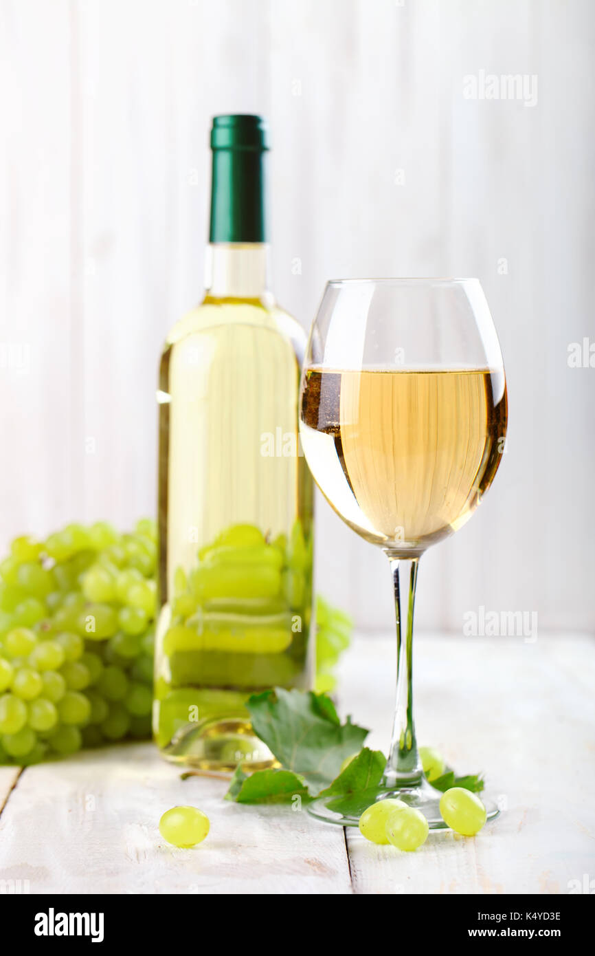 Un bicchiere di vino bianco, uve fresche e una bottiglia di vino bianco su di un tavolo di legno. Foto Stock