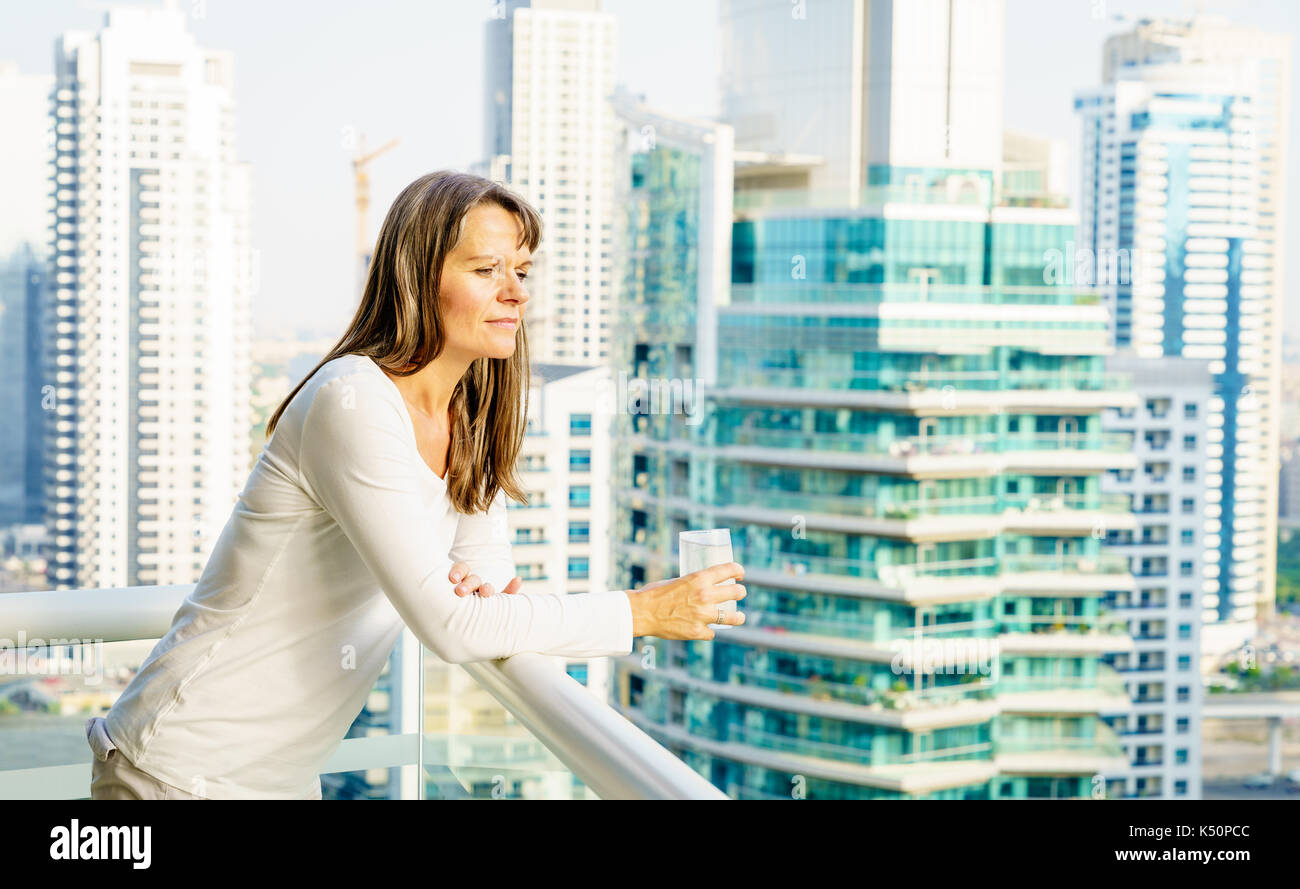 Donna matura è godendo città vista dal suo balcone in highrise building. Foto Stock