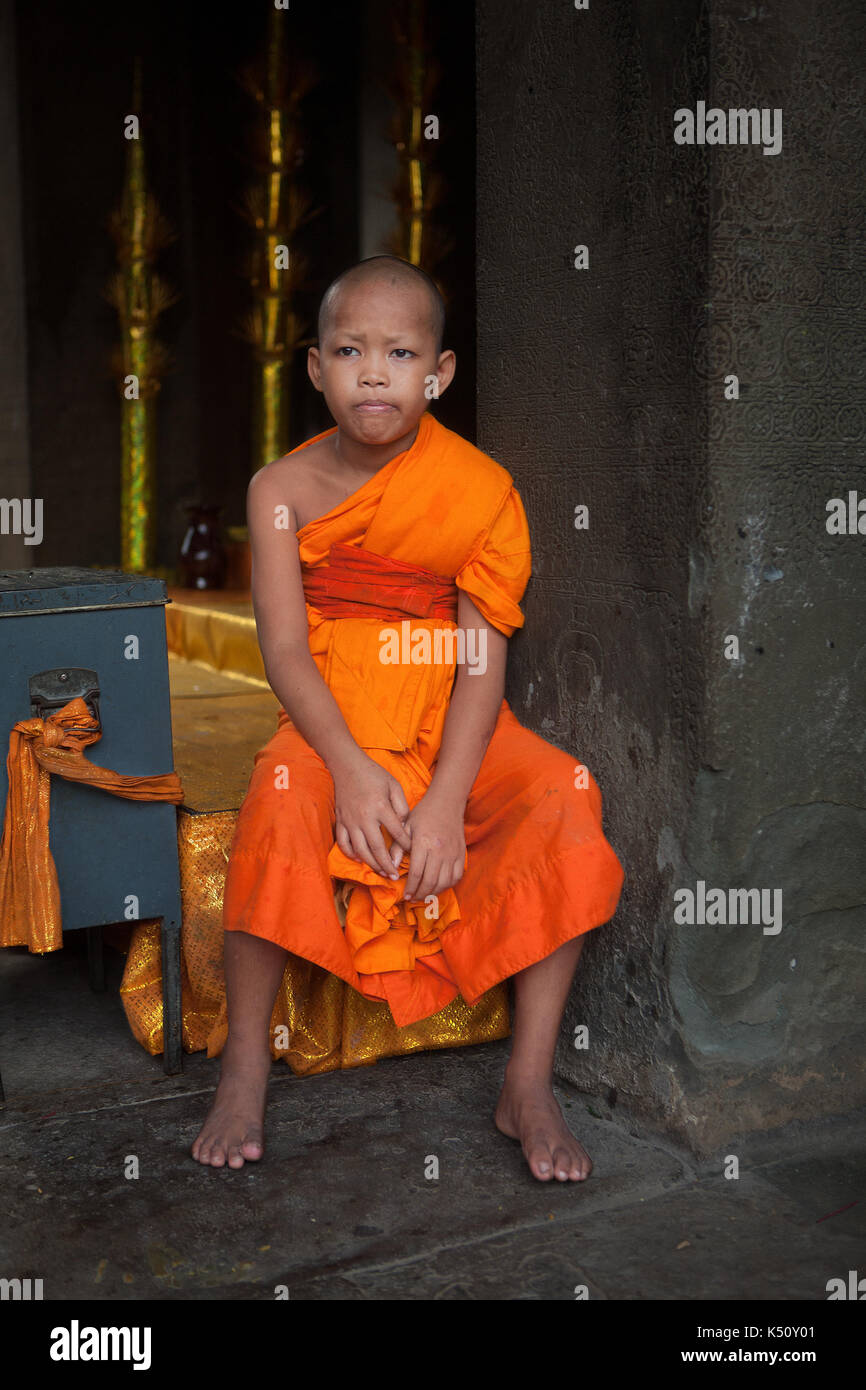 Un bummed out Theravada giovane monaco buddista infelice nel suo dovere di proteggere la casella di donazione a Angkor Wat in Siem Reap, Regno di Cambogia. Foto Stock