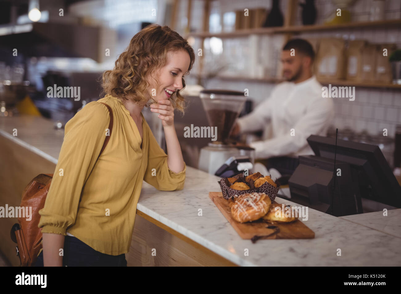 Sorridente giovane femmina cliente guardando il cibo nel servizio di bordo sul contatore presso la caffetteria Foto Stock