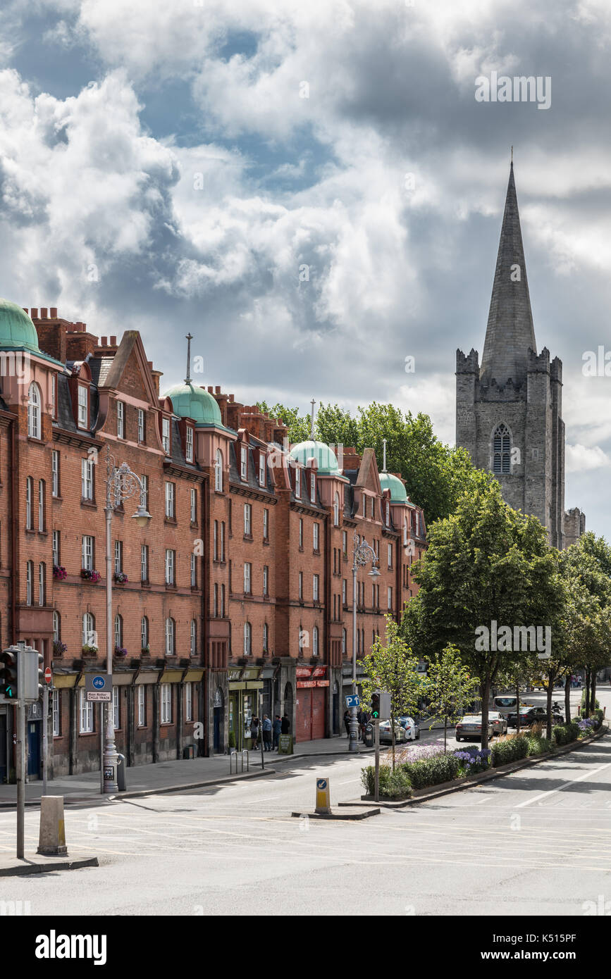Dublino, Irlanda - 7 agosto 2017: fila di mattoni rossi di facciate in Patrick Street che conduce a guglia della cattedrale di san patrizio. alberi verdi e il traffico li Foto Stock