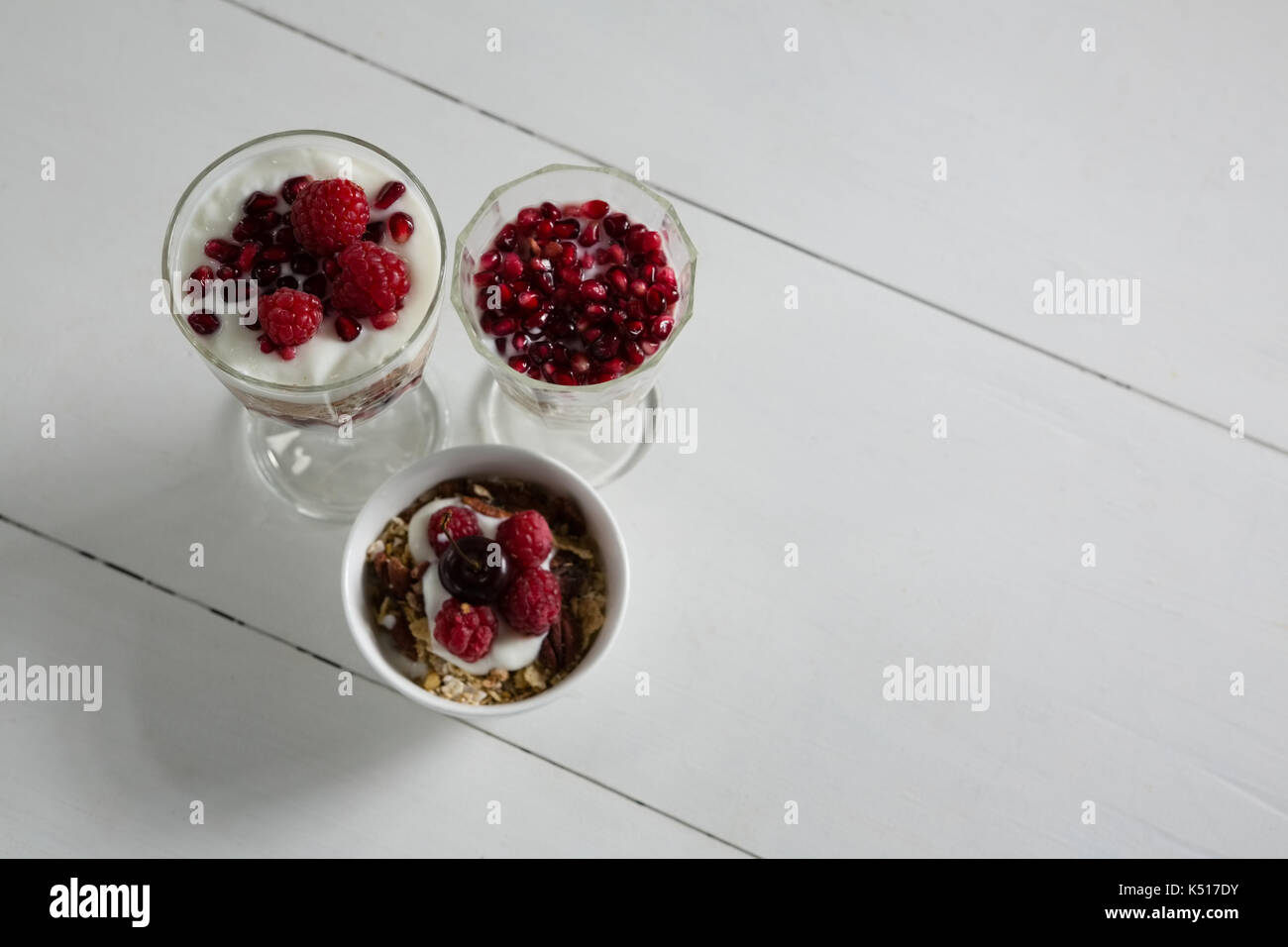 3 tazze di yogurt con lamponi e i semi di melograno su sfondo bianco Foto Stock
