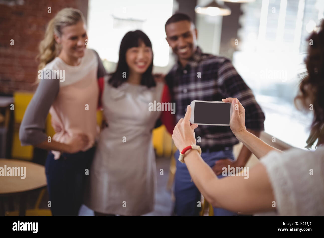 Immagine ritagliata della donna fotografa amici dallo smartphone al coffee shop Foto Stock