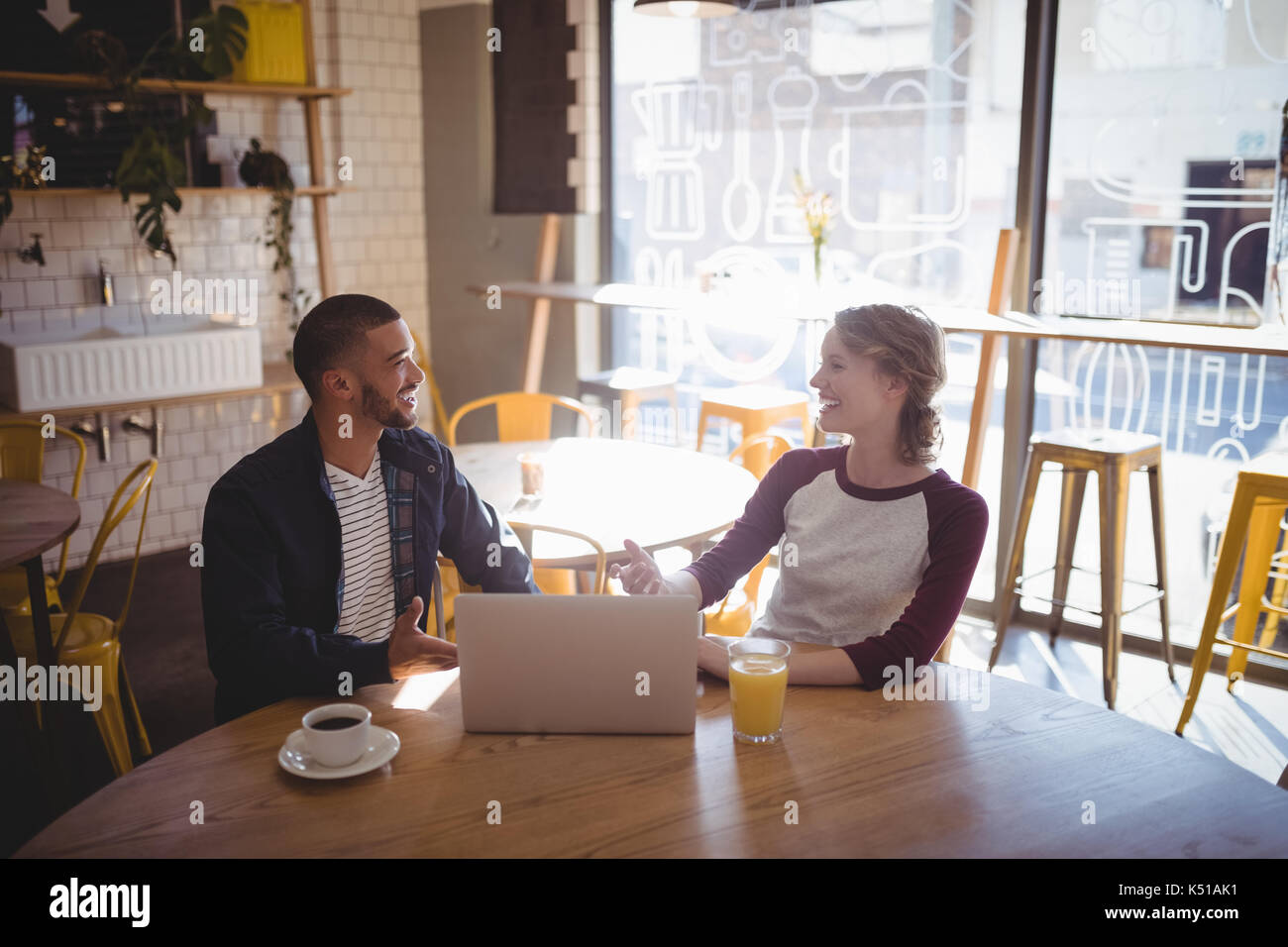 Sorridente giovani amici di parlare mentre è seduto con il portatile a tavola in coffee shop Foto Stock