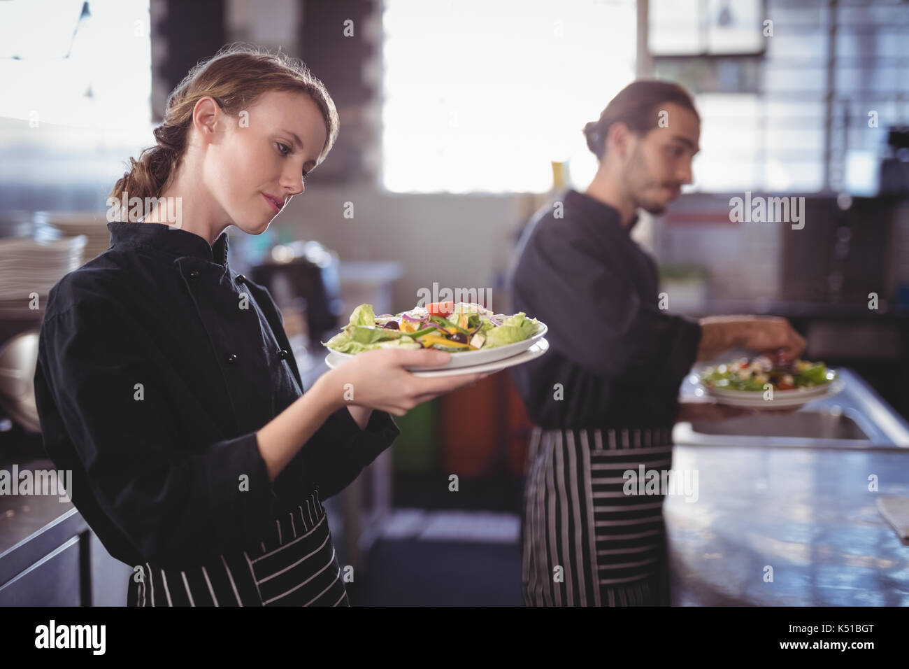 Giovani camerieri holding insalata fresca piastre mentre è in piedi in cucina commerciale presso la caffetteria Foto Stock