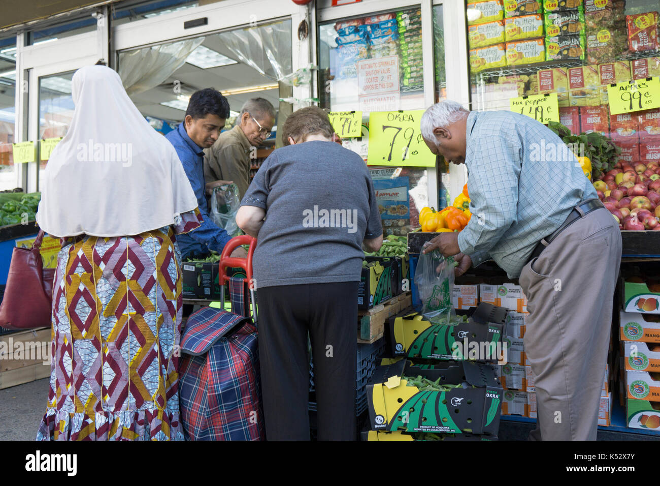 Un gruppo eterogeneo di persone acquista in vendita okra ad un stand esterno sulla 37th Ave. in Jackson Heights, Queens, a New York City. Foto Stock