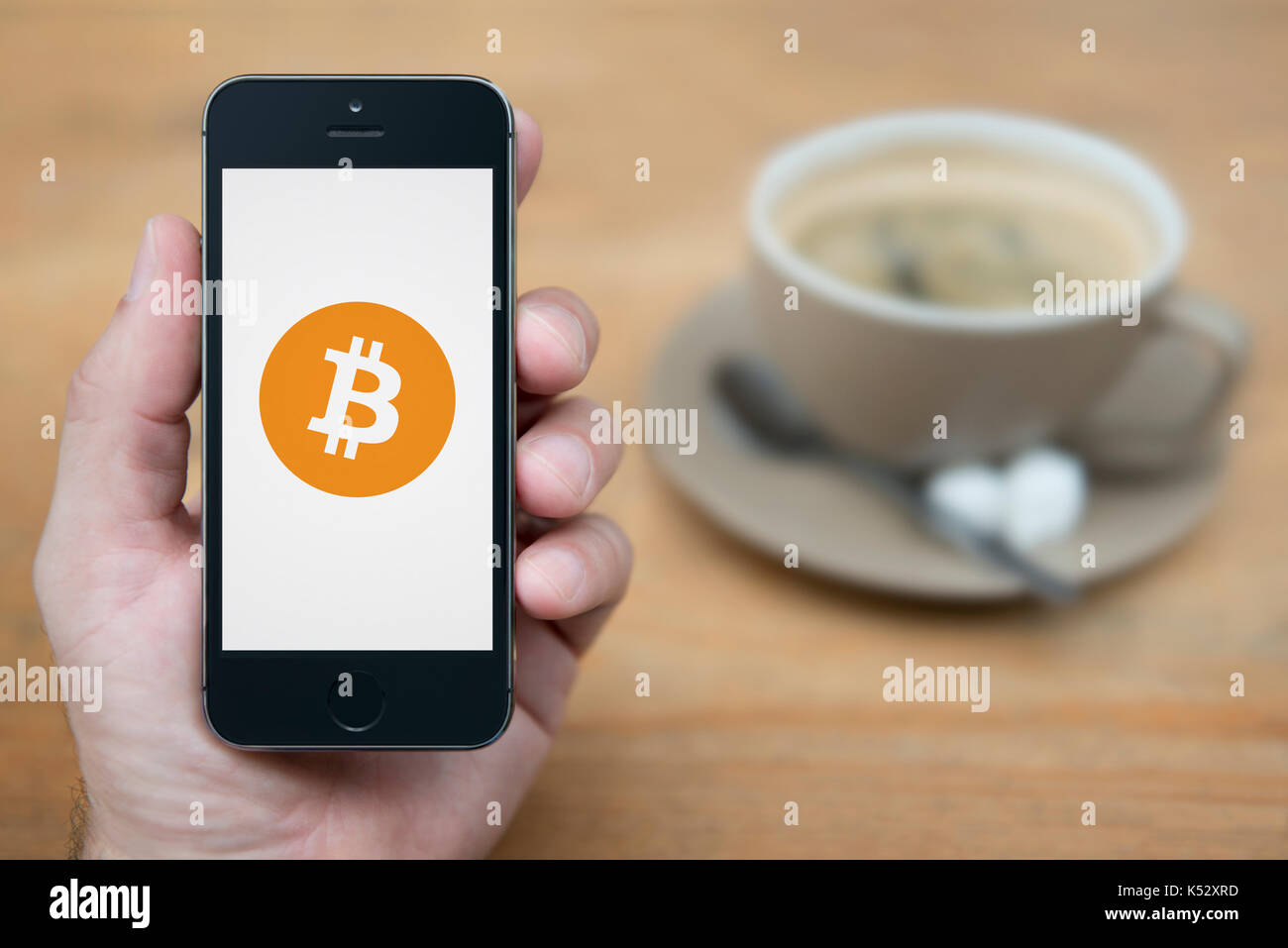 Un uomo guarda al suo iPhone che visualizza il logo Bitcoin (solo uso editoriale). Foto Stock