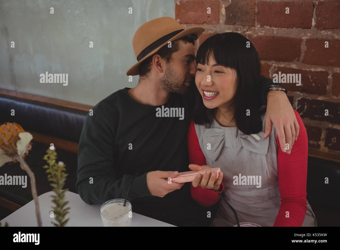 Giovane uomo whispering in donna orecchio mentre è seduto presso il cafe Foto Stock