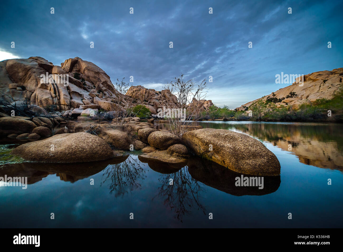Barker dam a Joshua Tree National Park, durante il crepuscolo. rocce di grandi dimensioni in primo piano circondato dall'acqua. Foto Stock