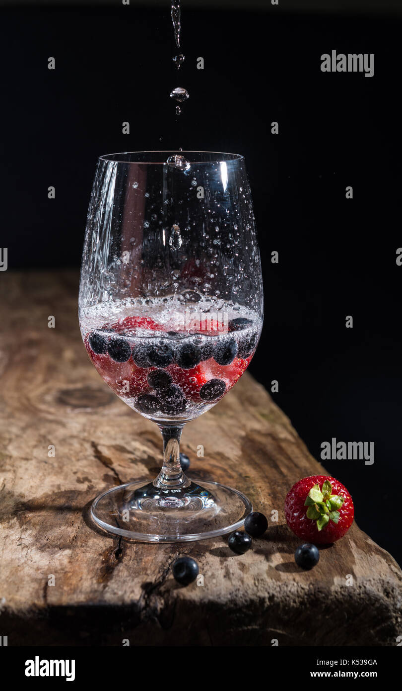 Bicchiere di acqua frizzante con fragole fresche e mirtilli, sgocciolatura di acqua in vetro Foto Stock