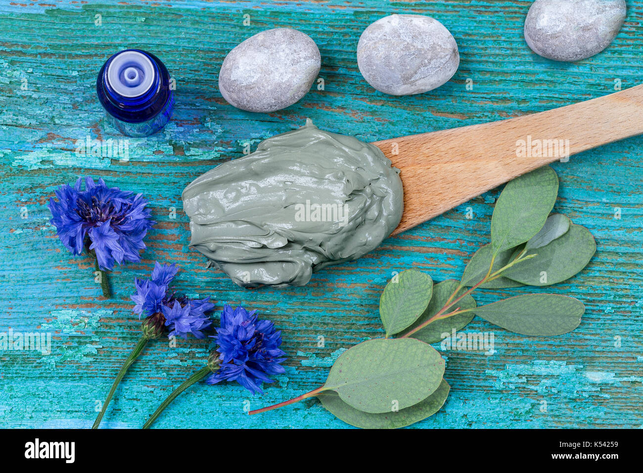 Olio essenziale di argilla di cosmetici e di fiordaliso e il ramo di eucalipto, pietre, per trattamenti spa, in cucchiaio di legno, sul vecchio blu sullo sfondo di legno Foto Stock