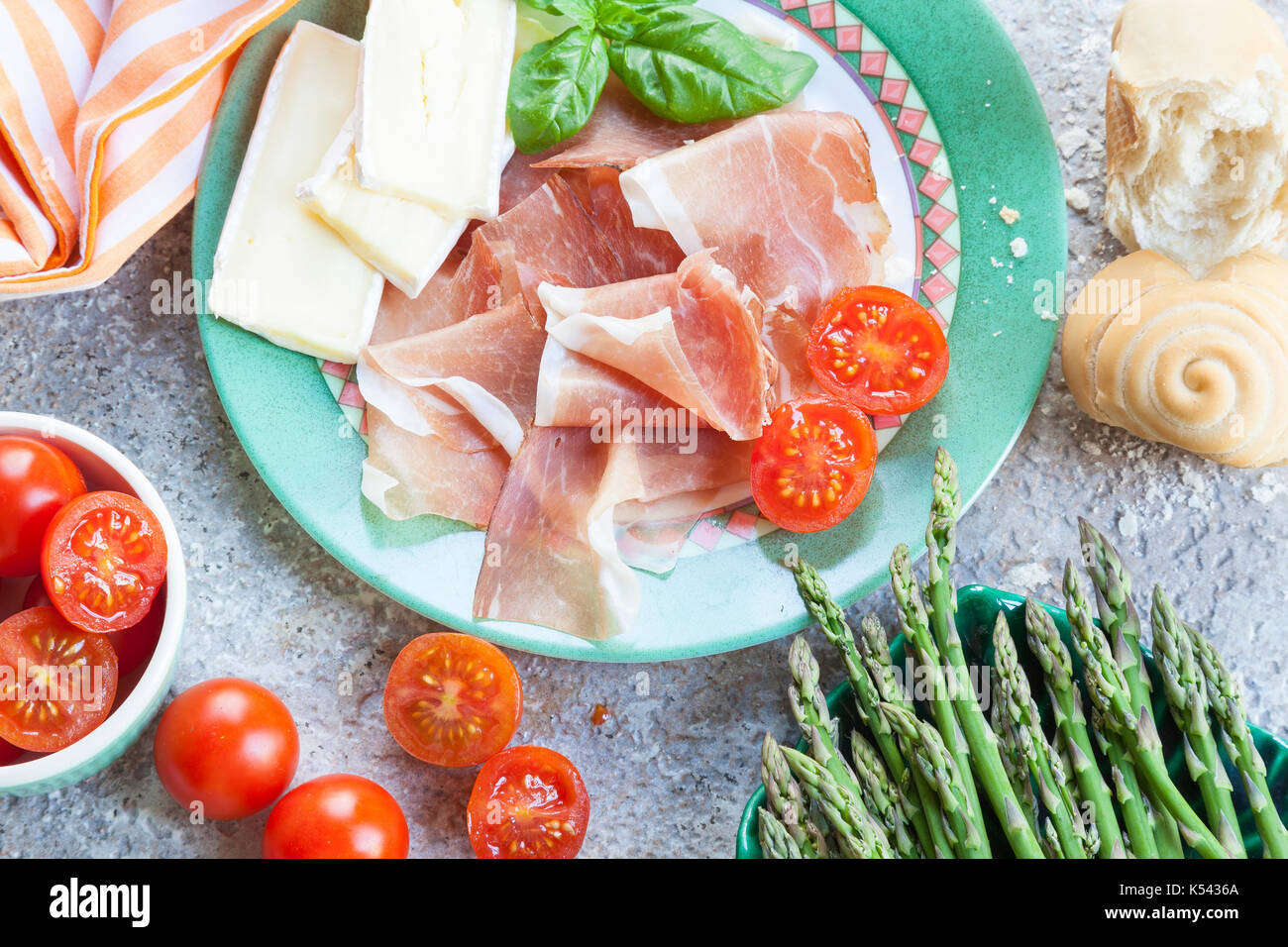 Delizioso pasto italiano di crudo Il prosciutto crudo, freschi Asparagi verdi spears, Formaggio Brie e pomodorini servita con pane appena sfornato roll Foto Stock