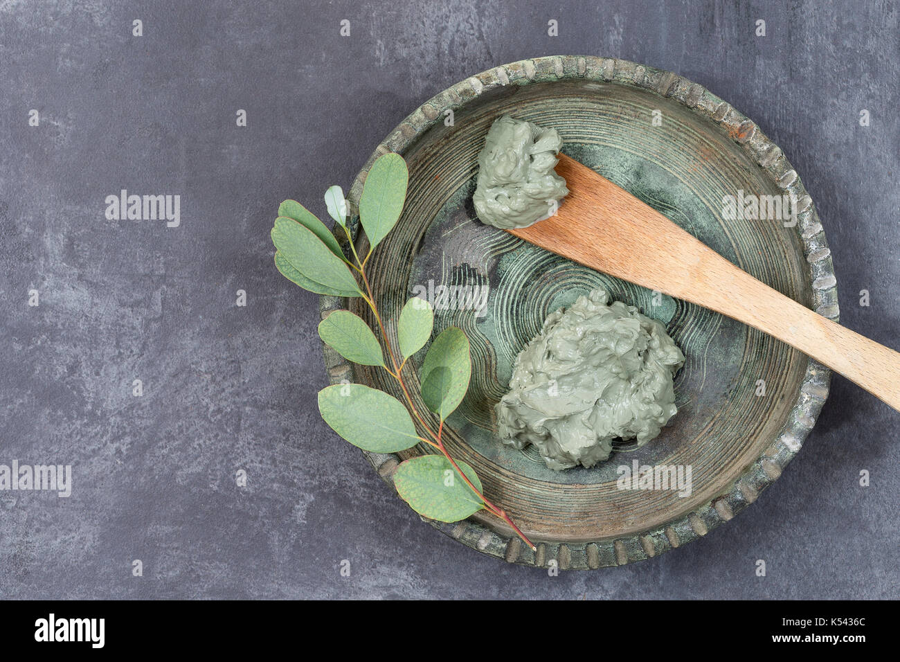 Olio essenziale di argilla di cosmetici e di fiordaliso e il ramo di eucalipto, pietre, per trattamenti spa, in cucchiaio di legno, sul vecchio blu sullo sfondo di legno Foto Stock