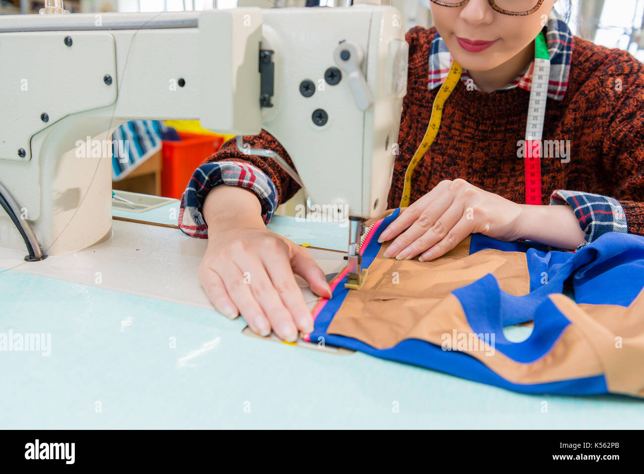 Giovane bella donna designer mani tenendo la progettazione di abbigliamento campione e cucitura filo colorato con macchina su misura in studio di moda. Foto Stock